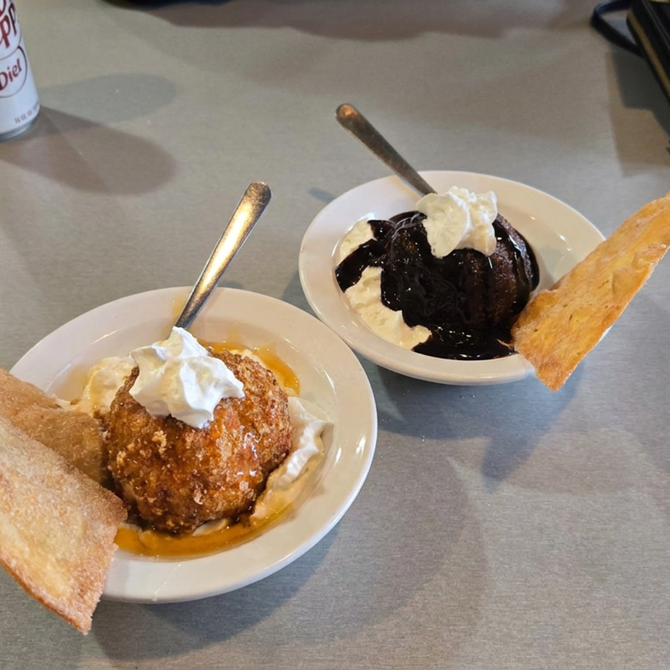 Two plated desserts with whipped cream, chocolate sauce, crispy pastry, and a soda on a restaurant table.