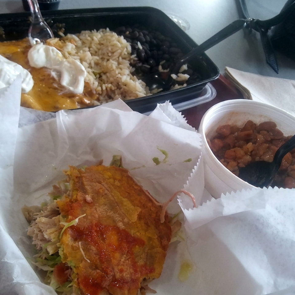 Takeout meal featuring a crispy sauced entrée over rice, beans, and vegetables, with a side of stewed beans and a second rice-and-beans plate.